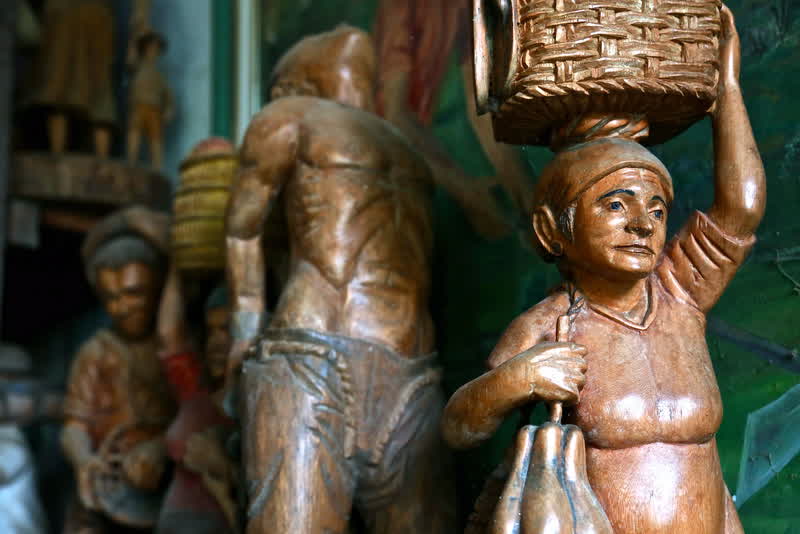 Esculturas de madeira representando figuras populares carregando cestos