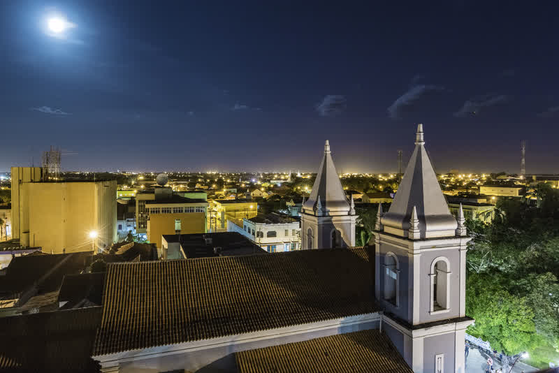 Vista noturna da cidade com as torres de uma igreja iluminadas em primeiro plano