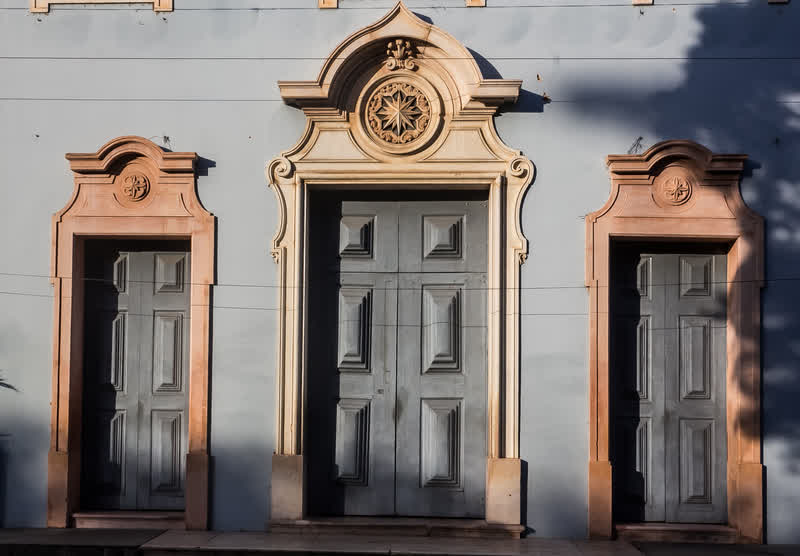 Fachada histórica com três portas de madeira emolduradas por ornamentos em relevo