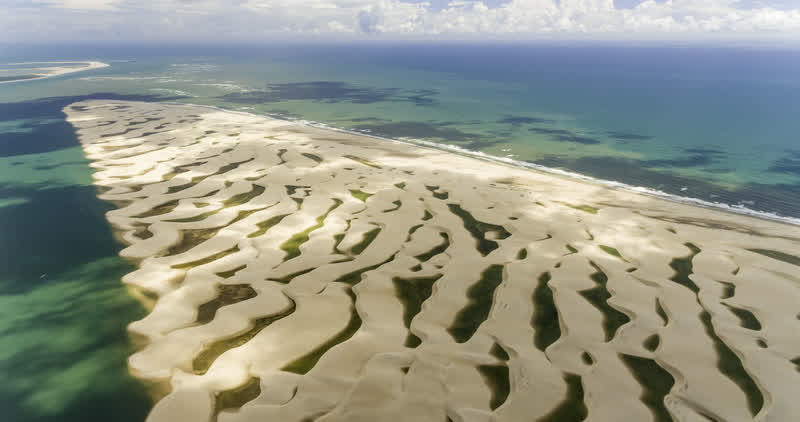 Vista aérea de uma faixa de dunas brancas entre o mar e lagoas esverdeadas
