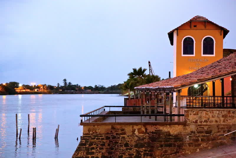 Casarão histórico com torre laranja à margem do rio ao entardecer