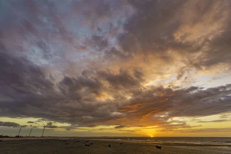 Pôr do sol dourado sob um céu cheio de nuvens em uma praia extensa