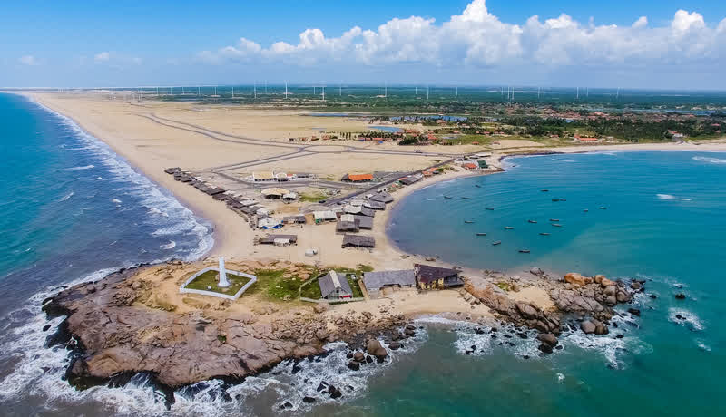 Vista aérea de uma ponta rochosa com farol entre duas praias, uma de mar calmo e outra de mar agitado