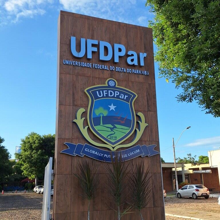 Totem de entrada da UFDPar com o nome e o brasão da universidade, sob céu azul